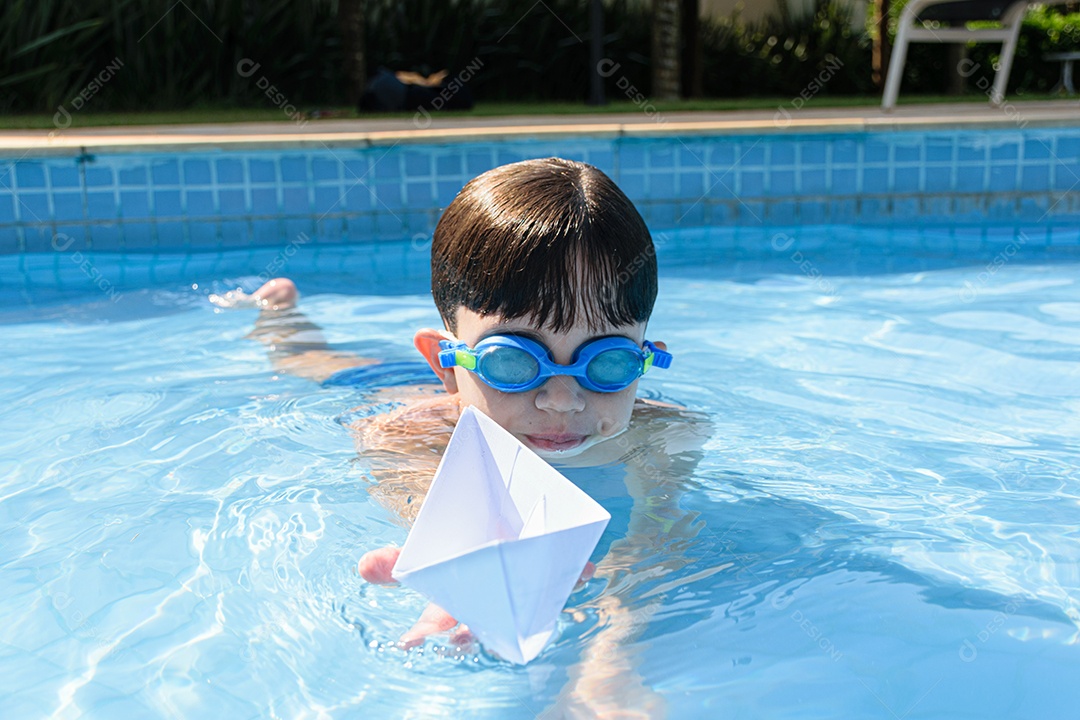 Criança na piscina destruindo o barquinho de papel com o punho.