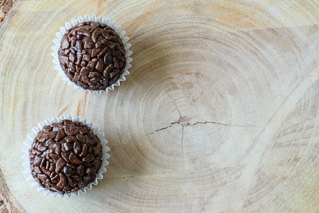 Brigadeiros de chocolate granulados alinhados em tábuas de madeira.