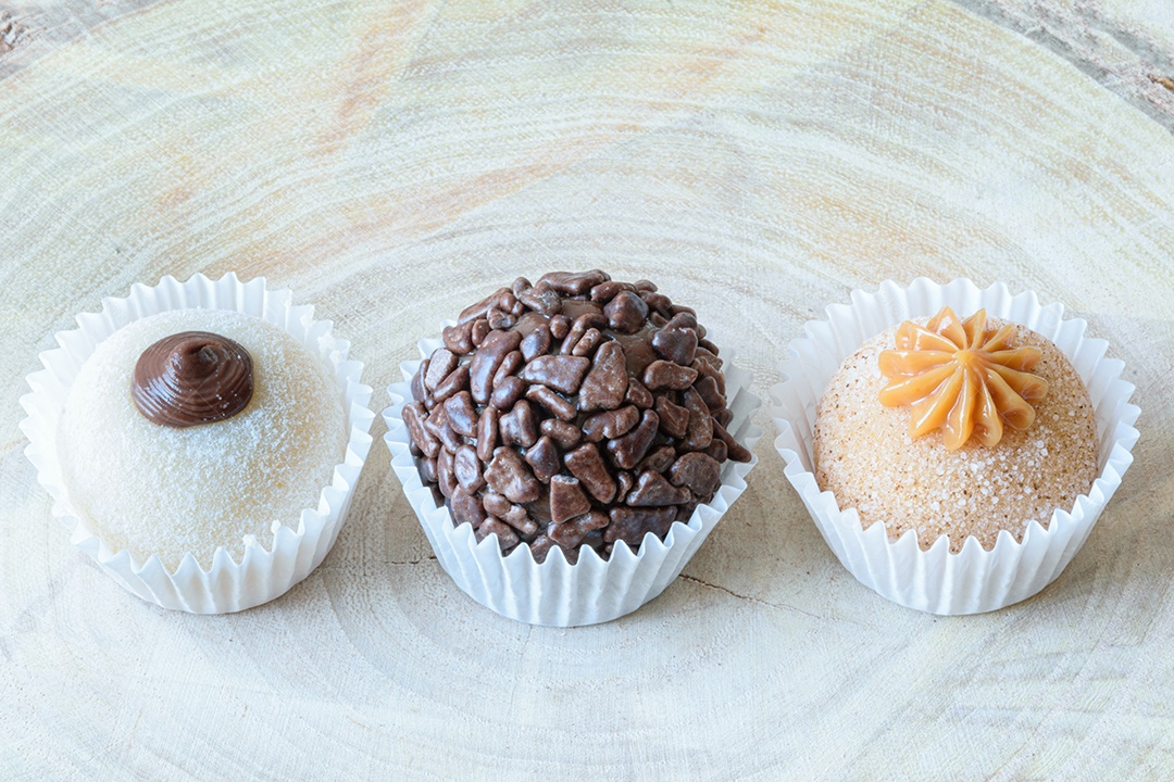Detalhe de três brigadeiros diferentes em uma tábua de madeira.