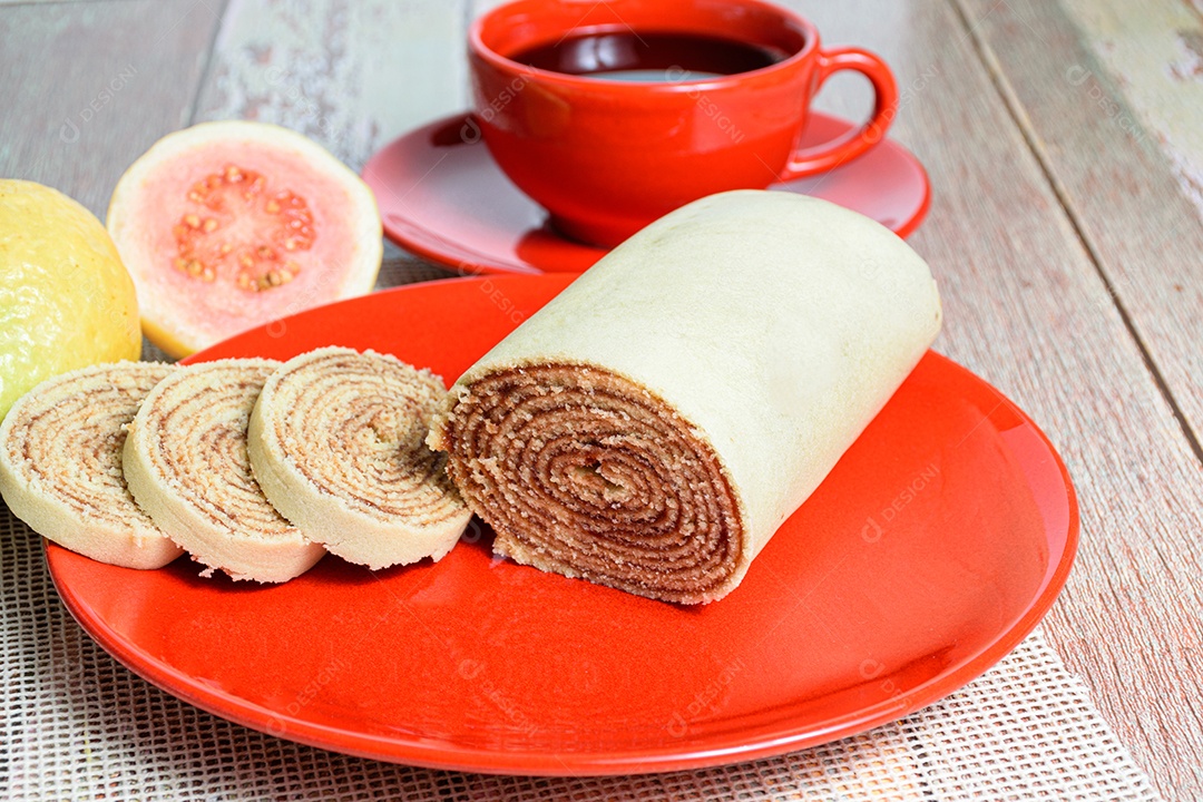 Bolo de rolo fatiado em prato vermelho ao lado de goiabas.