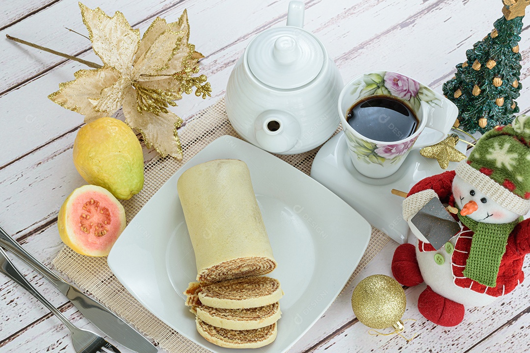 Bolo de rolo fatiado em prato vermelho ao lado de goiabas.