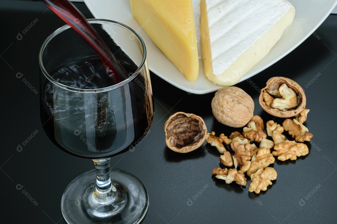 Nozes ao lado de uma taça de vinho tinto, queijo parmesão e queijo brie.