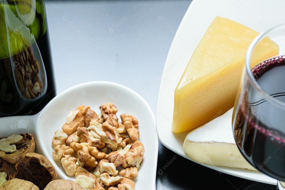 Nozes ao lado de uma taça de vinho tinto, queijo parmesão e queijo