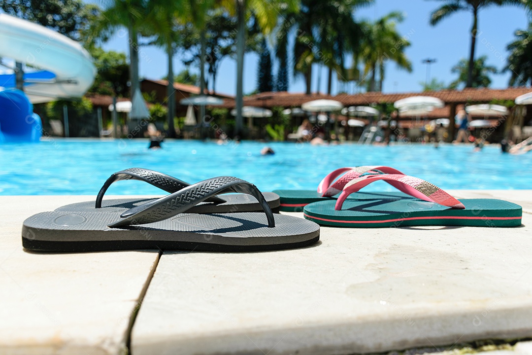 Dois pares de chinelos na beira da piscina em um dia ensolarado.