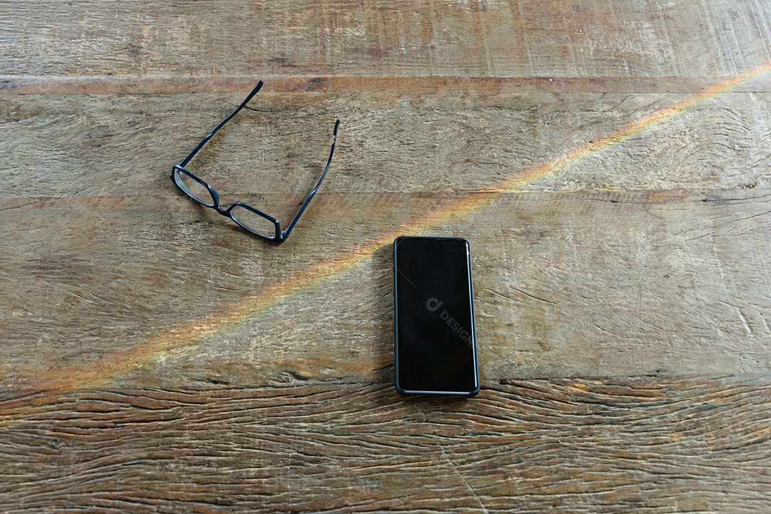 Smartphone em uma mesa de madeira. Ambos, sendo atravessados ​​por um raio de sol.