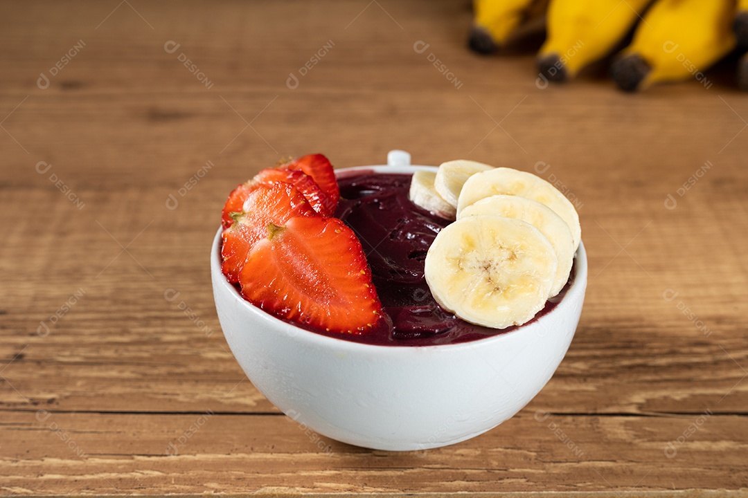 Tigela branca de açaí brasileiro congelado com paçoca, morango e banana.