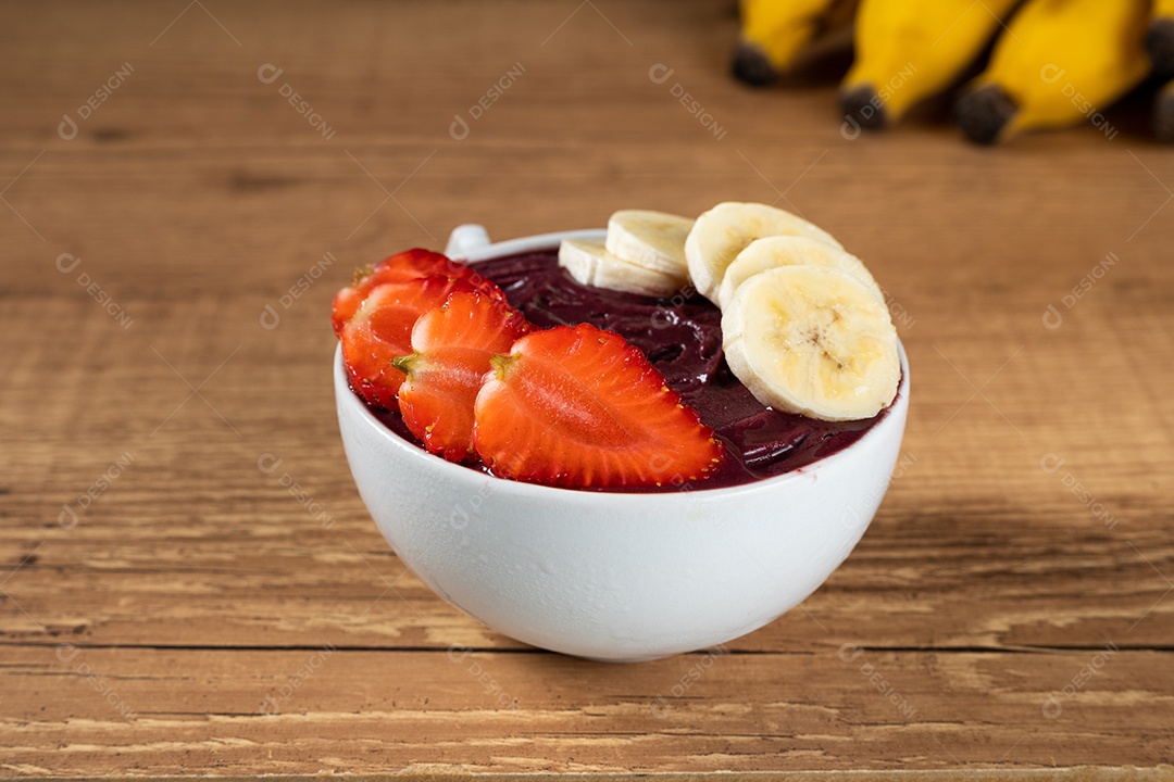 Tigela branca de açaí brasileiro congelado com paçoca, morango e banana.