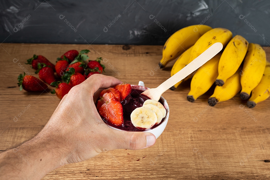 Mão segurando uma tigela de açaí brasileira com banana e morango