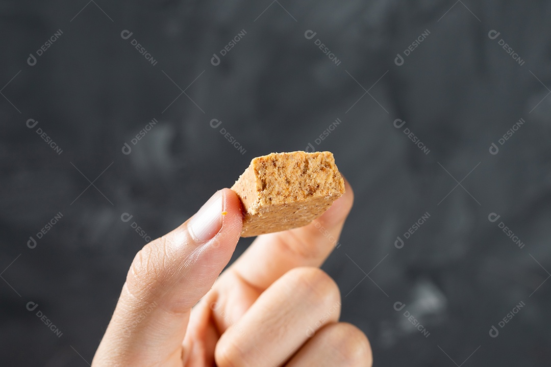 Dedos segurando um Doce de Amendoim Brasileiro chamado Paçoca.