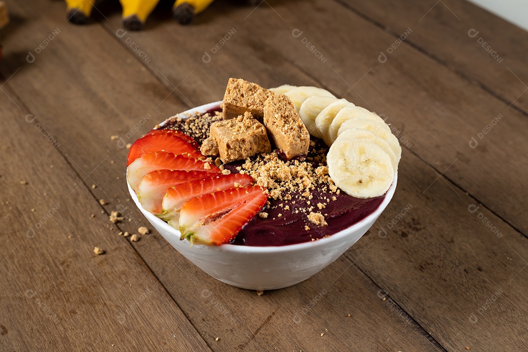 Tigela branca de açaí brasileiro congelado com paçoca, morango e banana.