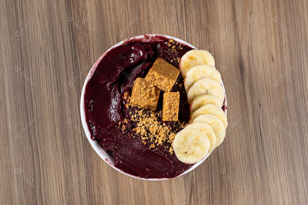 Tigela branca de açaí brasileiro congelado com paçoca, morango e banana.