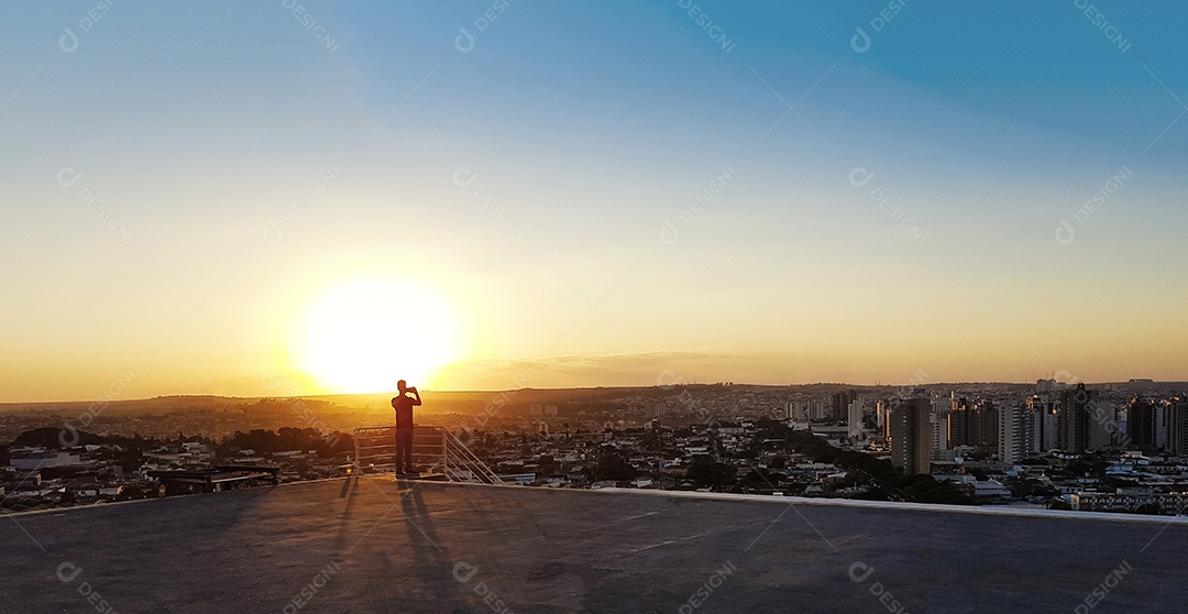 Silhueta de um homem no topo de um edifício por do sol