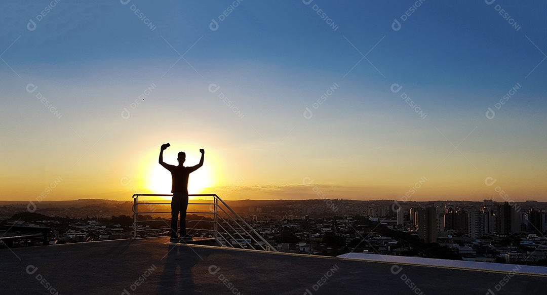 Silhueta de um homem no topo de um edifício por do sol
