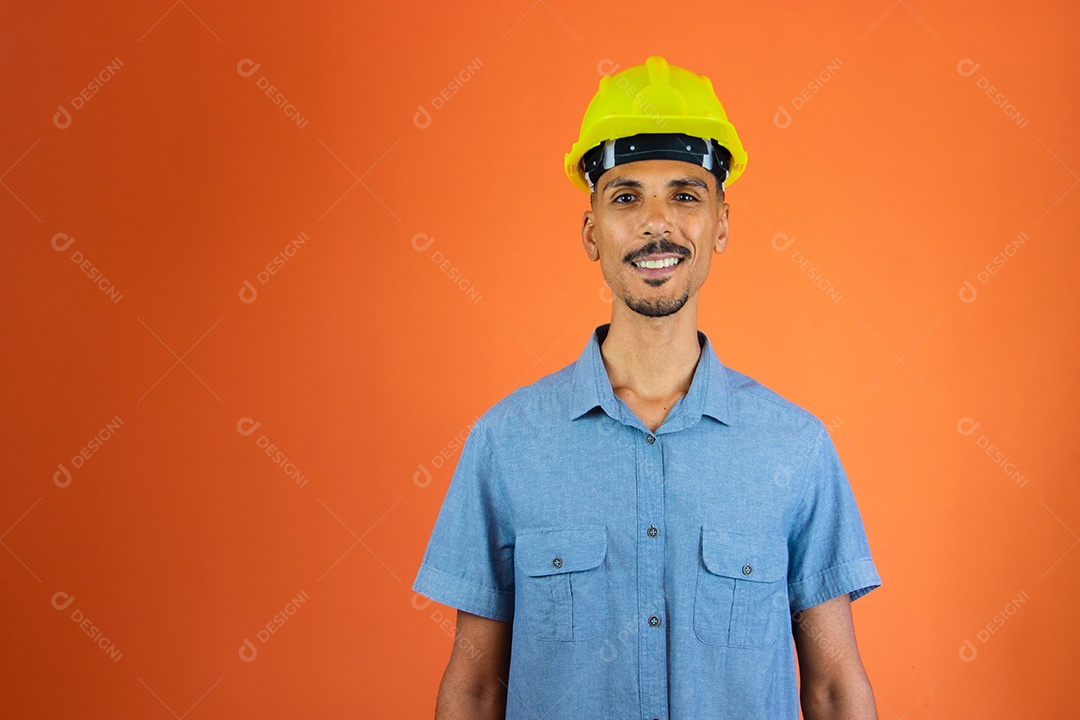 Homem negro no capacete de segurança e camisa azul isolada em laranja.