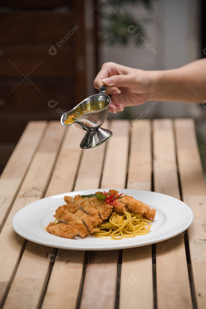 Mãos de pessoa colocando macarronada sobre prato branco mesa madeira