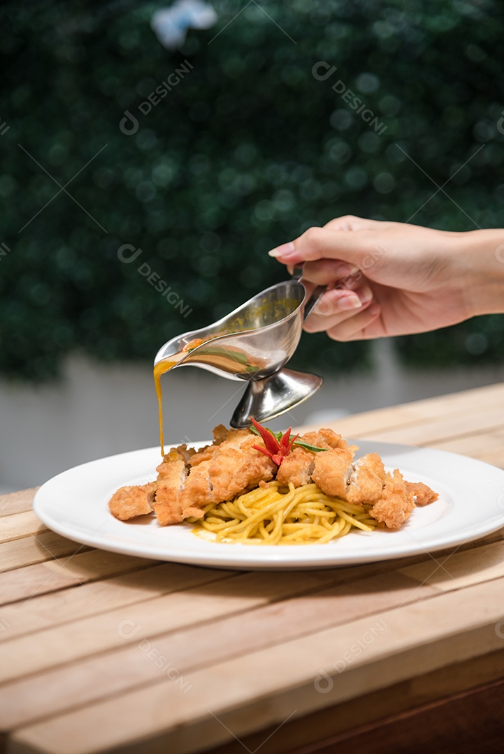 Mãos de pessoa colocando macarronada sobre prato branco mesa madeira