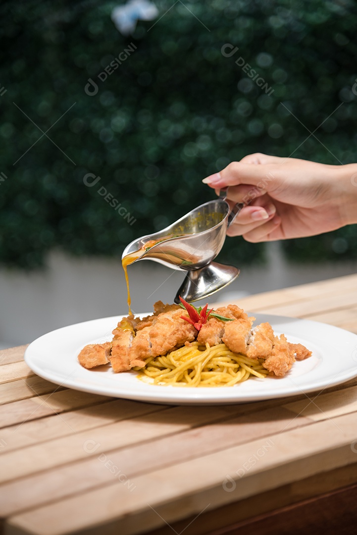 Mãos de pessoa colocando macarronada sobre prato branco mesa madeira