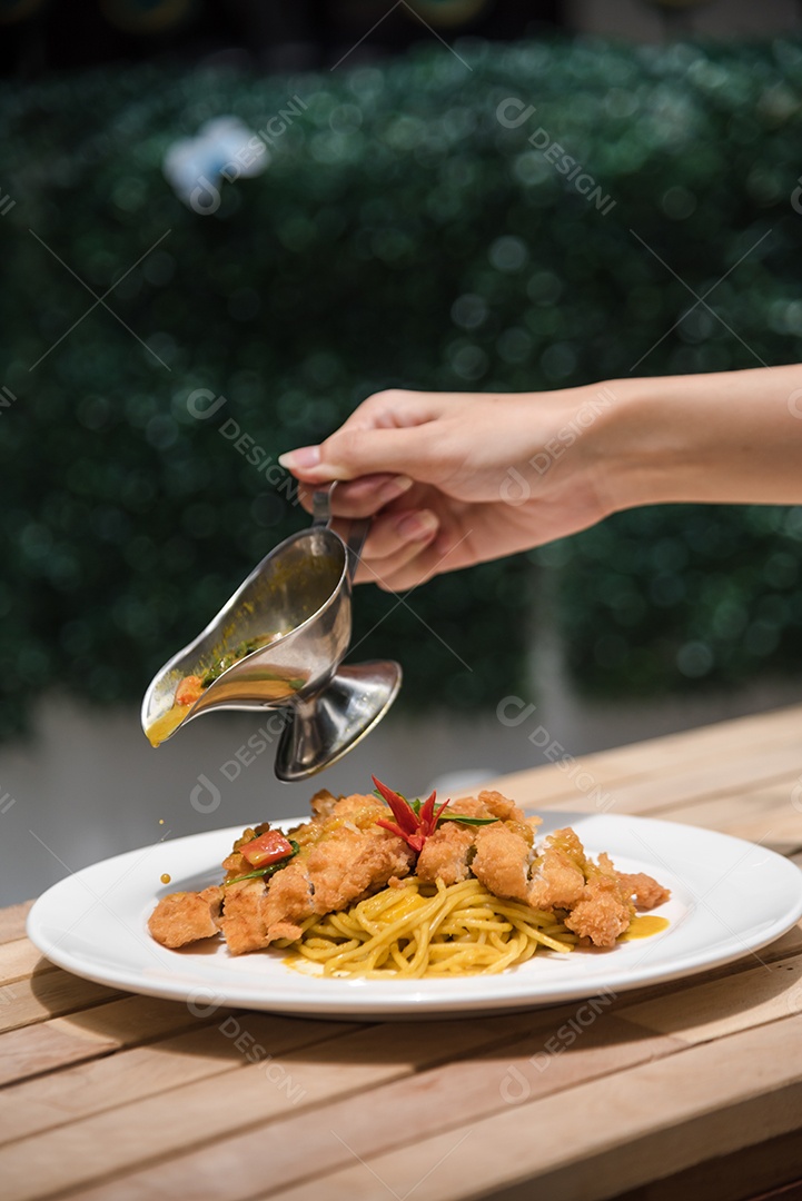 Mãos de pessoa colocando macarronada sobre prato branco mesa madeira
