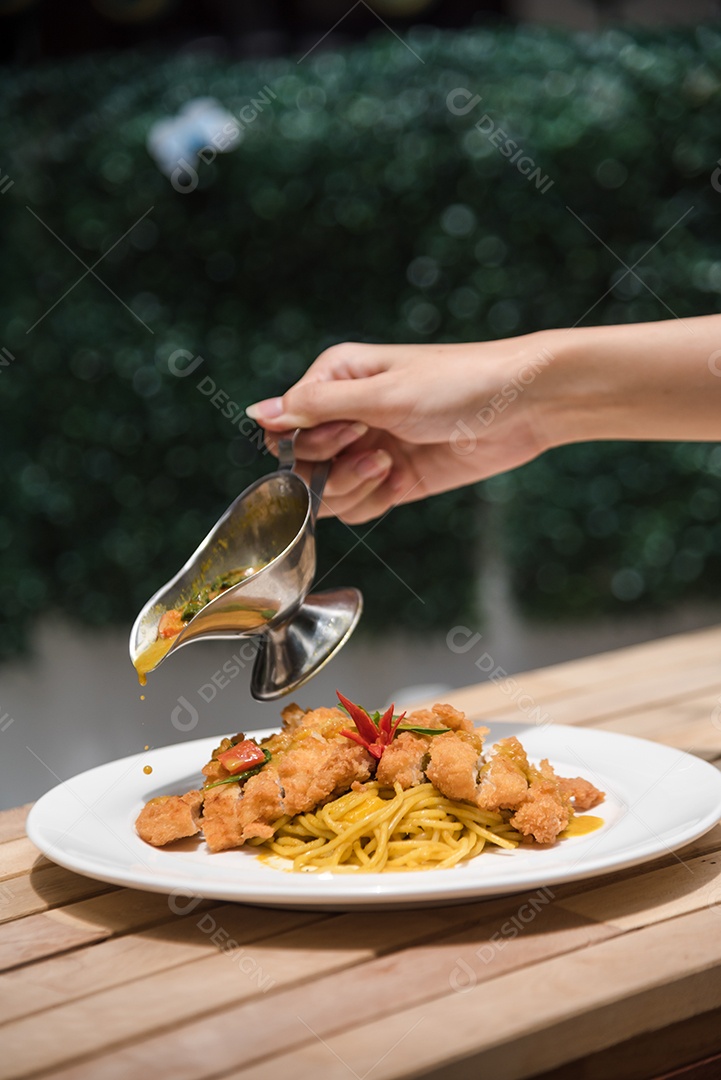 Mãos de pessoa colocando macarronada sobre prato branco mesa madeira