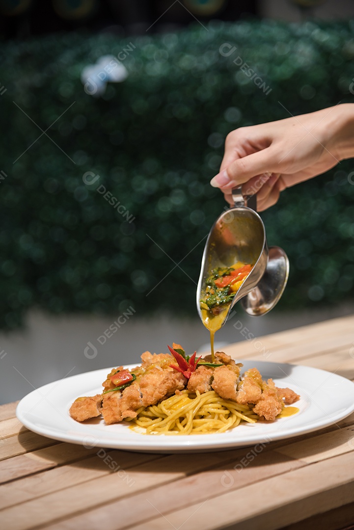 Mãos de pessoa colocando macarronada sobre prato branco mesa madeira