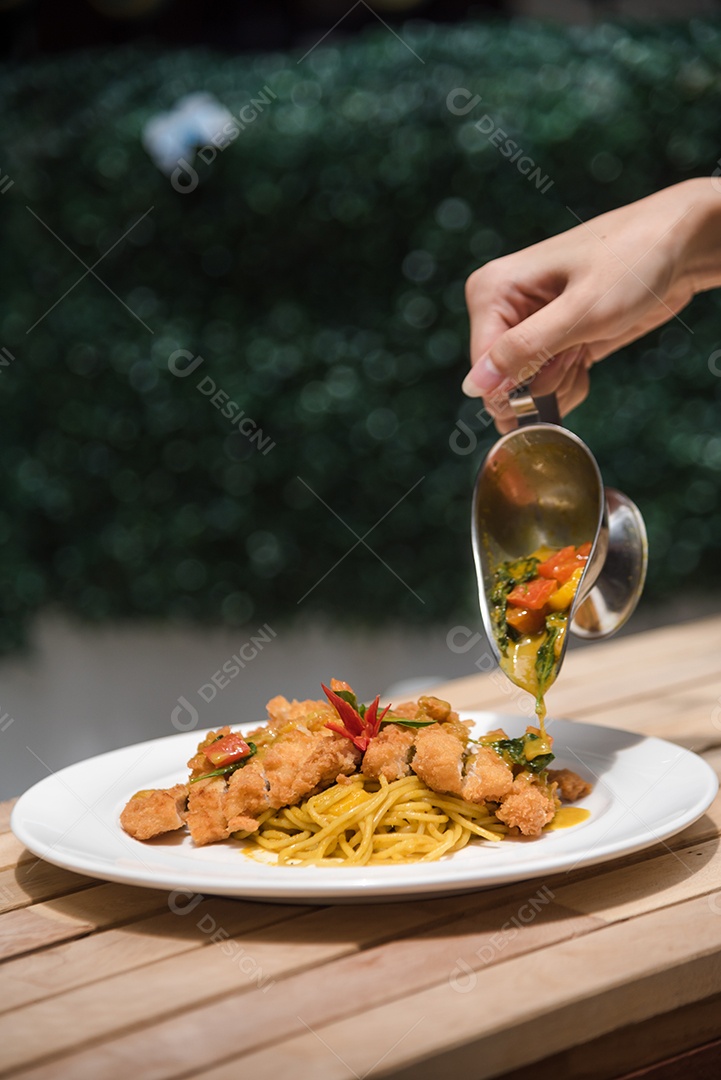 Mãos de pessoa colocando macarronada sobre prato branco mesa madeira