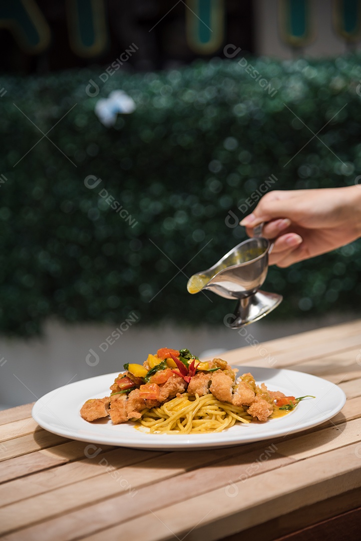 Mãos de pessoa colocando macarronada sobre prato branco mesa madeira