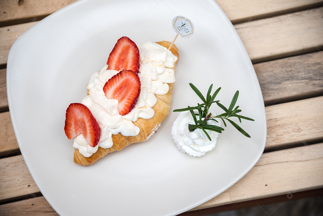 Pão sobre prato branco chantily morango cortado em feitas sobre uma mesa madeira
