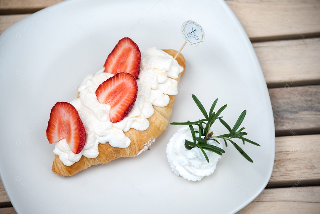 Pão sobre prato branco chantily morango cortado em feitas sobre uma mesa madeira