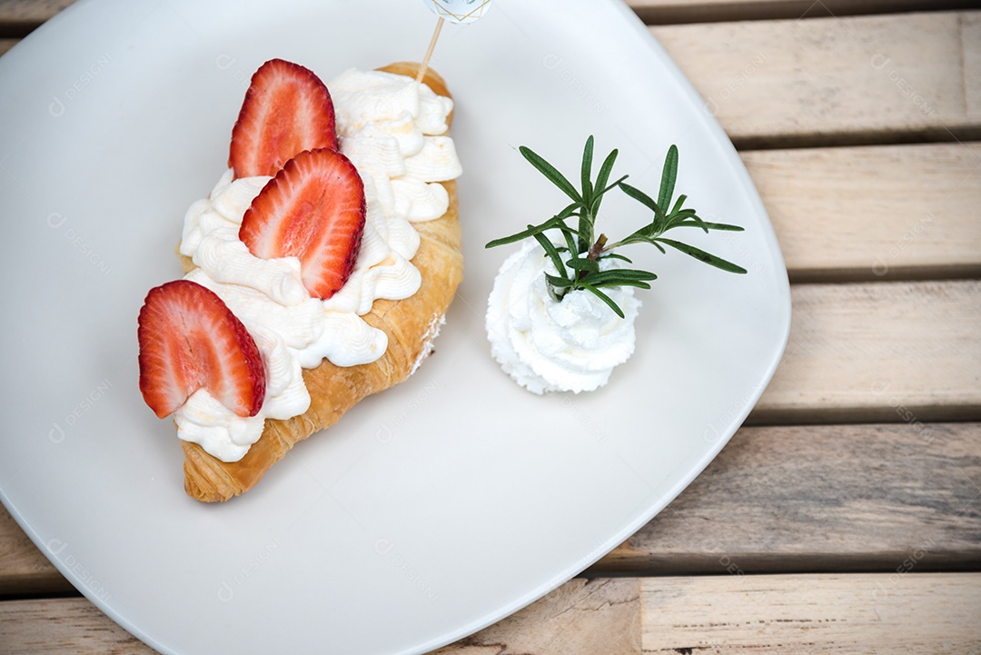 Pão sobre prato branco chantily morango cortado em feitas sobre uma mesa madeira