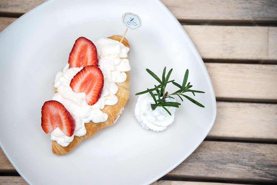 Pão sobre prato branco chantily morango cortado em feitas sobre uma mesa madeira