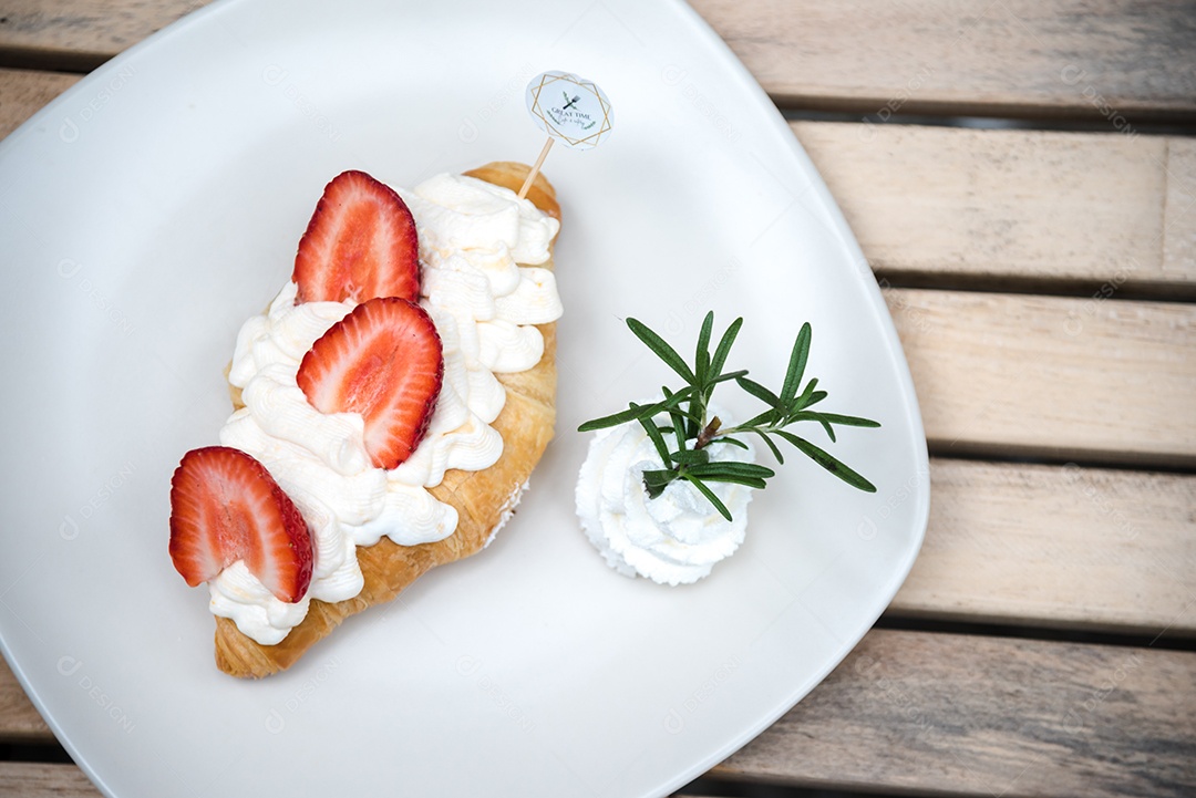 Pão sobre prato branco chantily morango cortado em feitas sobre uma mesa madeira