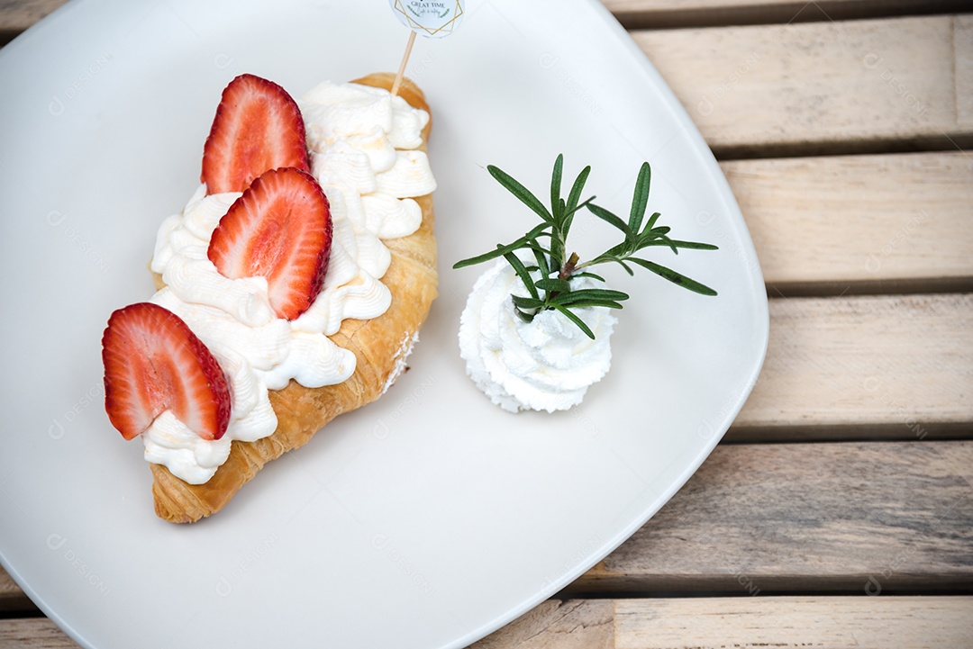 Pão sobre prato branco chantily morango cortado em feitas sobre uma mesa madeira