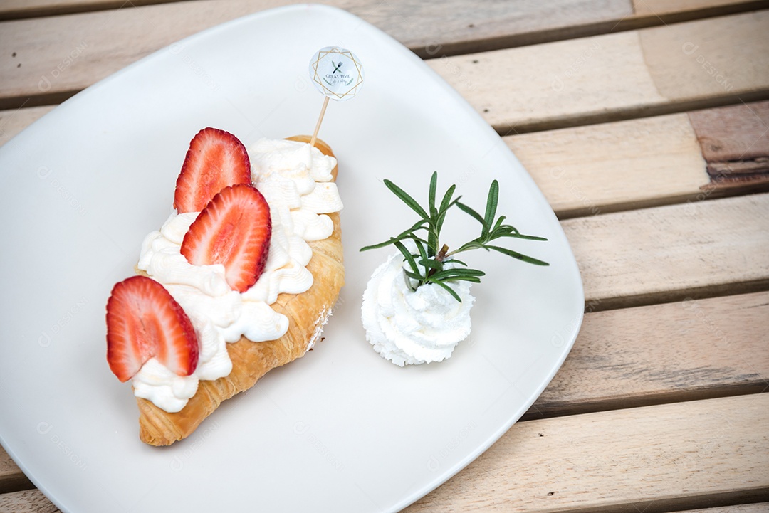 Pão sobre prato branco chantily morango cortado em feitas sobre uma mesa madeira