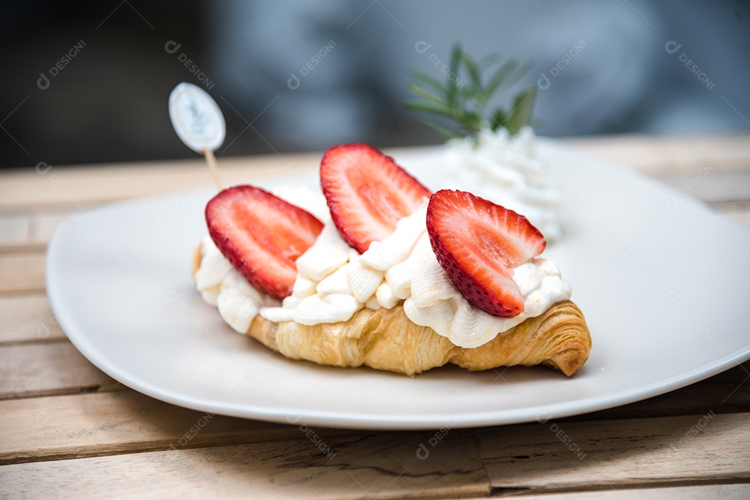 Pão sobre prato branco chantily morango cortado em feitas sobre uma mesa madeira