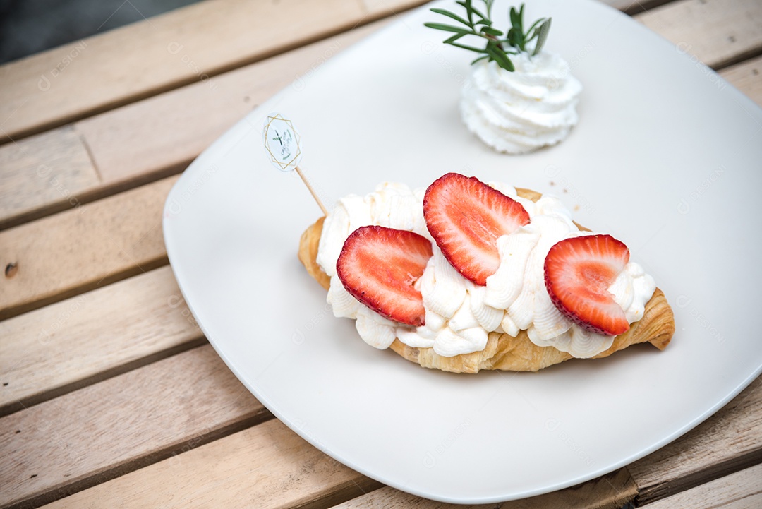 Pão sobre prato branco chantily morango cortado em feitas sobre uma mesa madeira