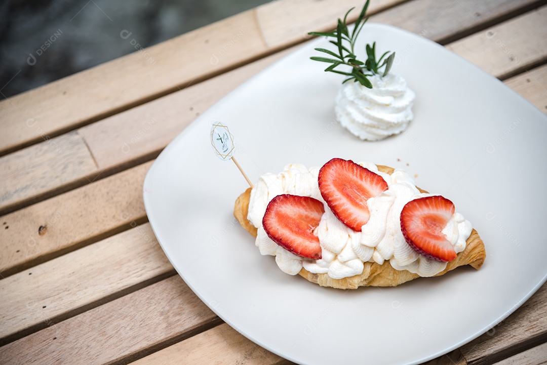 Pão sobre prato branco chantily morango cortado em feitas sobre uma mesa madeira
