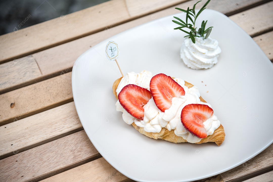 Pão sobre prato branco chantily morango cortado em feitas sobre uma mesa madeira