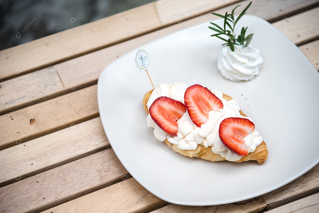 Pão sobre prato branco chantily morango cortado em feitas sobre uma mesa madeira