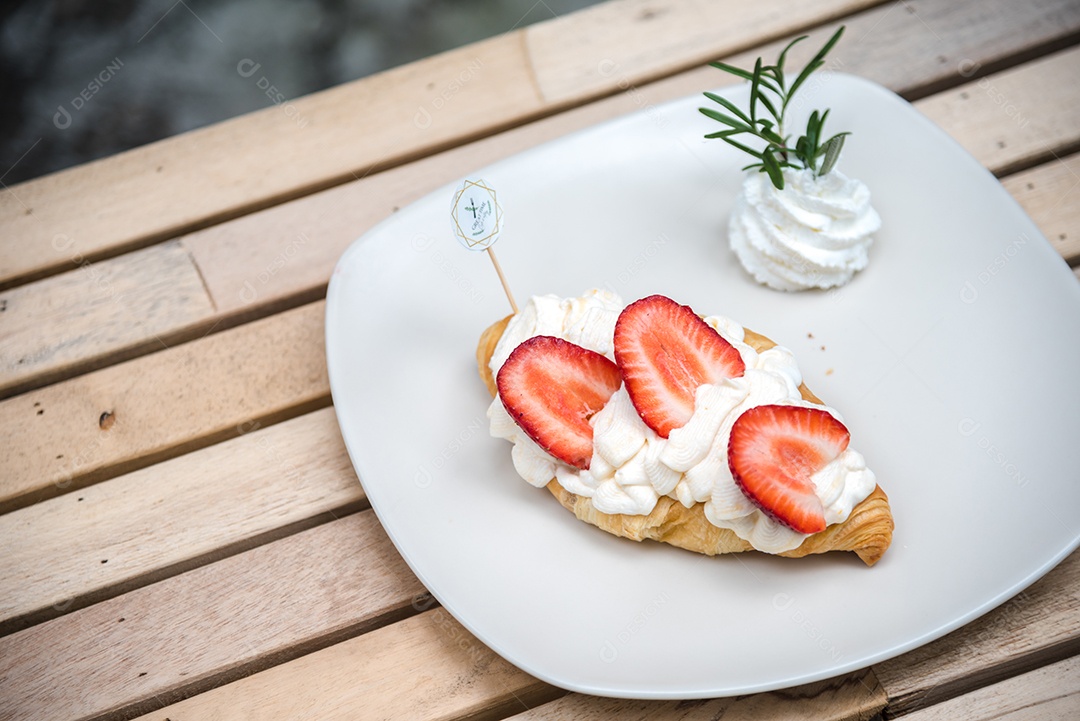 Pão sobre prato branco chantily morango cortado em feitas sobre uma mesa madeira