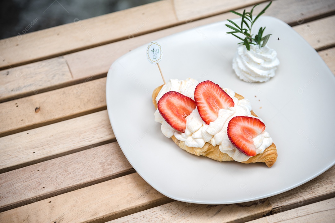 Pão sobre prato branco chantily morango cortado em feitas sobre uma mesa madeira