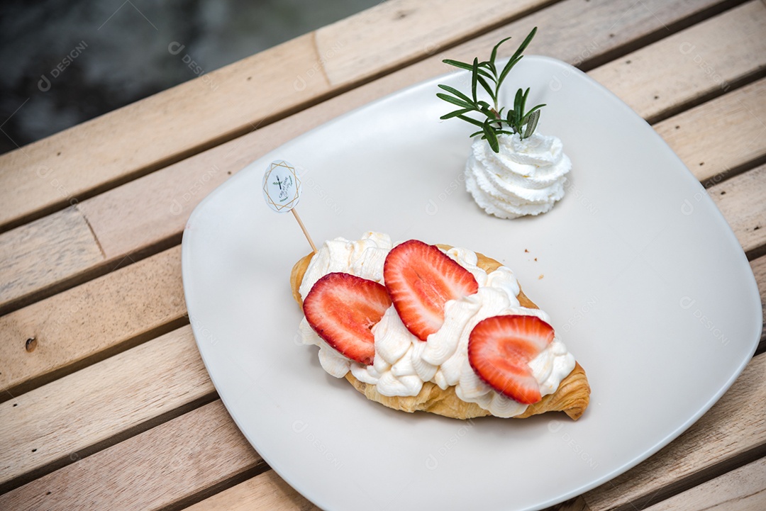 Pão sobre prato branco chantily morango cortado em feitas sobre uma mesa madeira