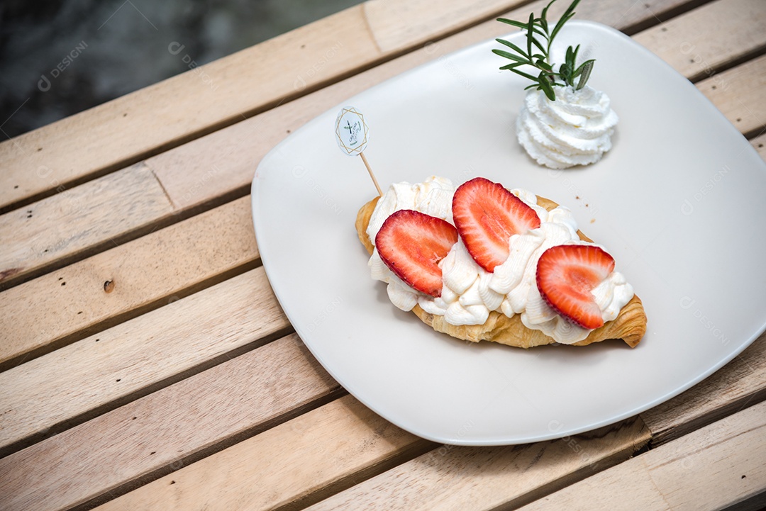 Pão sobre prato branco chantily morango cortado em feitas sobre uma mesa madeira