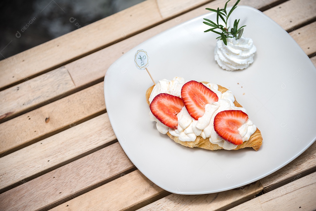 Pão sobre prato branco chantily morango cortado em feitas sobre uma mesa madeira
