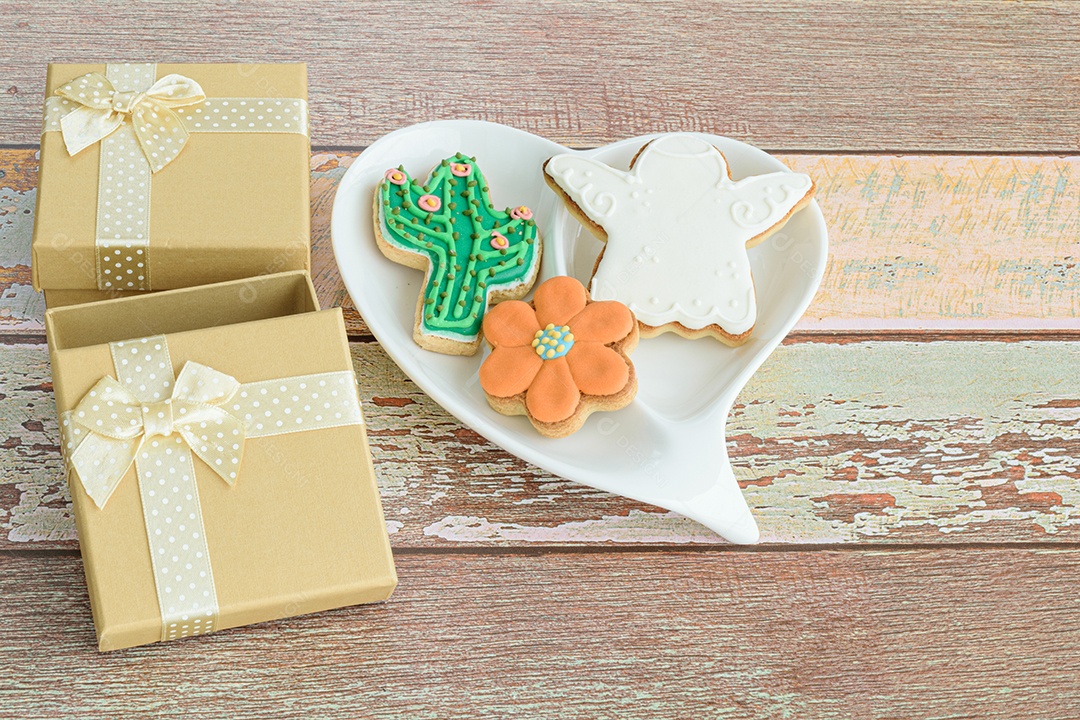 Biscoitos em forma de flor, cacto e anjo, ao lado de uma pequena caixa de presente