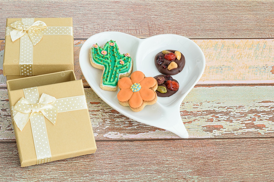 Biscoitos diferentes em um prato em forma de coração, ao lado de um pequeno presente