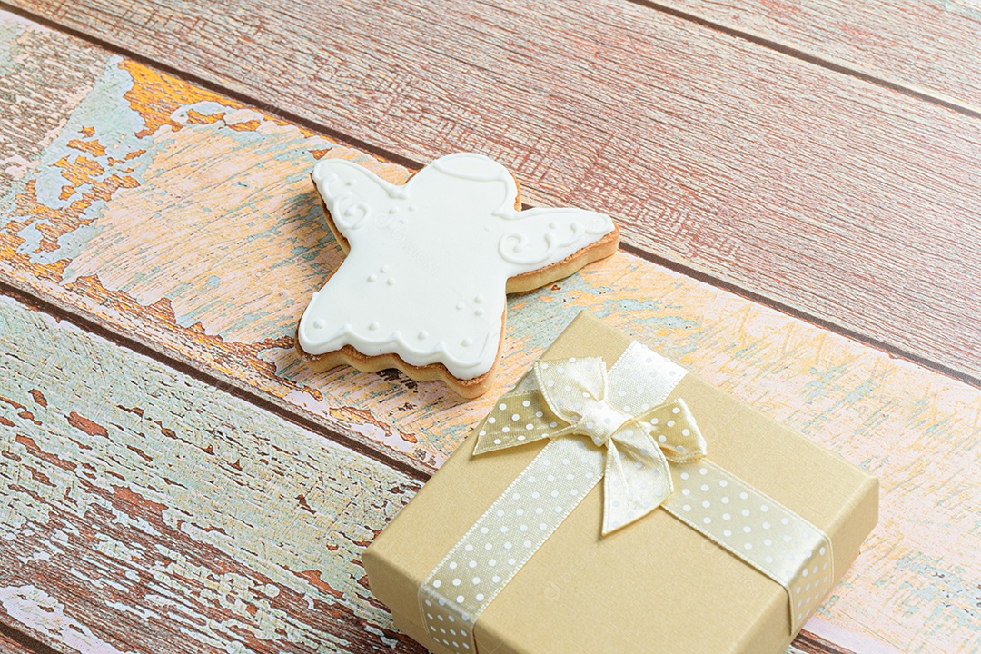 Biscoito em forma de anjo na mesa, ao lado de uma caixa de presente dourada.
