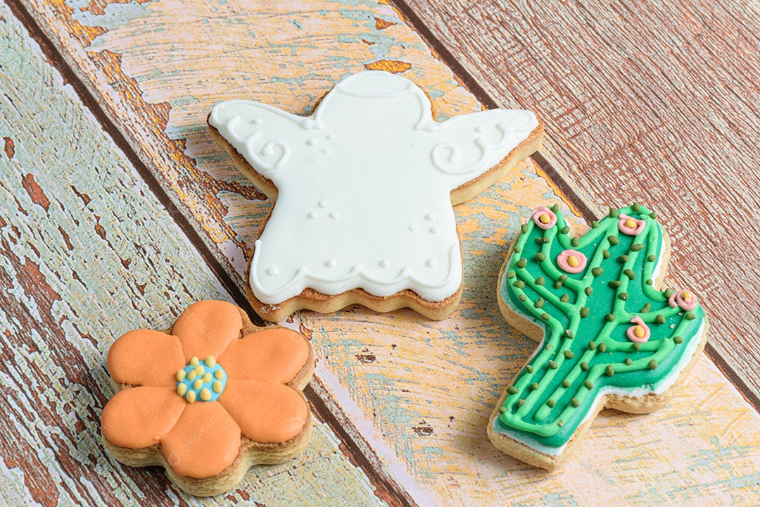 Biscoitos em forma de anjo, flor e cacto na mesa de madeira.