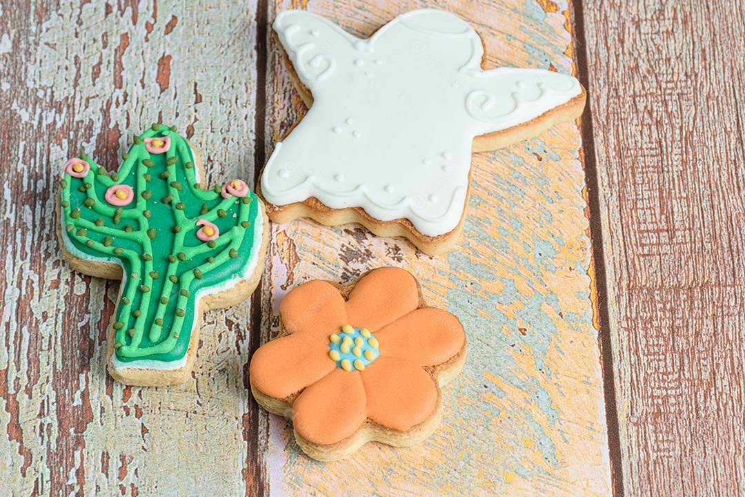 Biscoitos em forma de anjo, flor e cacto na mesa de madeira.