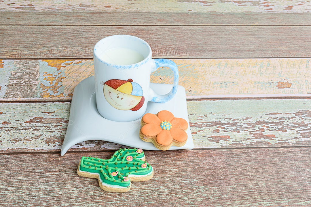 Dois biscoitos de formatos variados ao lado de uma pequena caneca de leite.