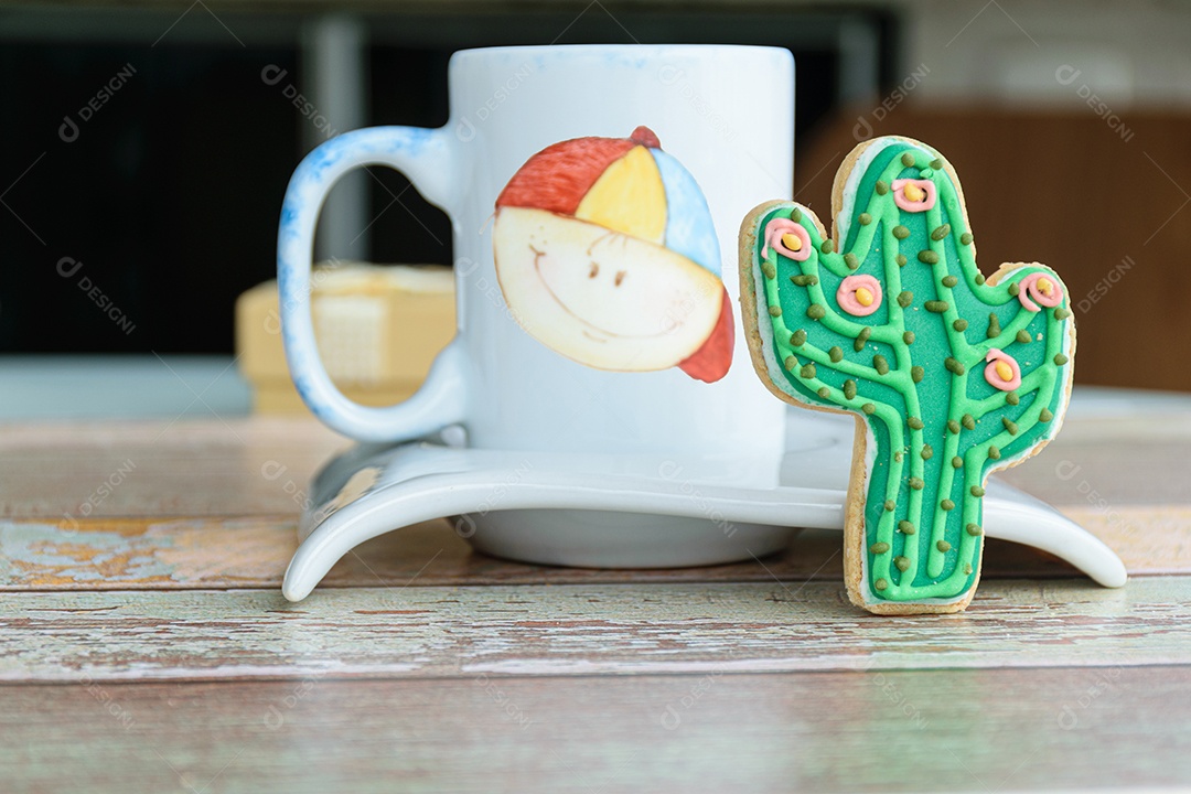 Biscoito em forma de cacto ao lado de uma pequena caneca de leite.